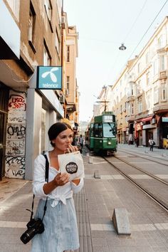 a woman is standing on the side walk with her hand in her mouth and looking at something