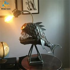 a metal fish sculpture sitting on top of a table next to a lamp and pictures