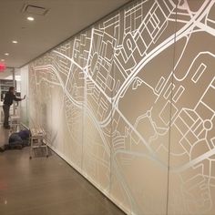 a man is standing in front of a wall with a map on it and people are walking by