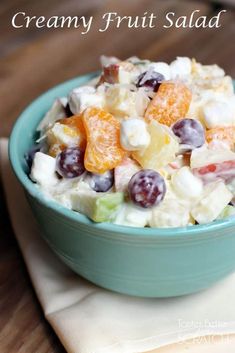 a blue bowl filled with fruit salad sitting on top of a wooden table next to a napkin