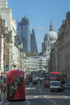 a red double decker bus driving down a busy street next to tall buildings and traffic lights