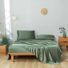 a bed with green sheets and pillows in a white room next to two nightstands