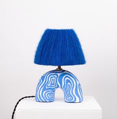 a table lamp with a blue shade sitting on top of a white block in front of a white wall