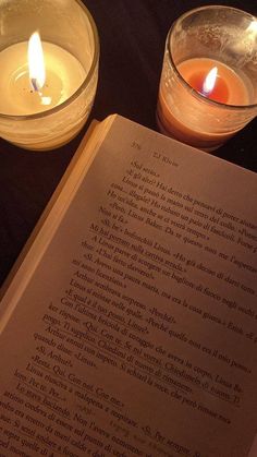 an open book sitting next to two lit candles