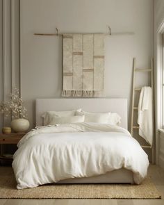 a white bed sitting in a bedroom next to a wall hanging on a wooden frame