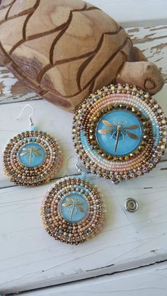 three pieces of beaded jewelry sitting on top of a white wooden table next to a vase