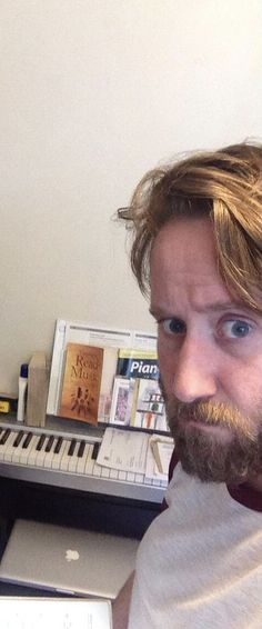 a man with long hair and beard sitting in front of a computer keyboard, looking at the camera