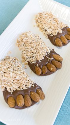 three almonds and chocolate covered cookies on a white plate