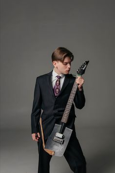 a young man in a suit holding an electric guitar