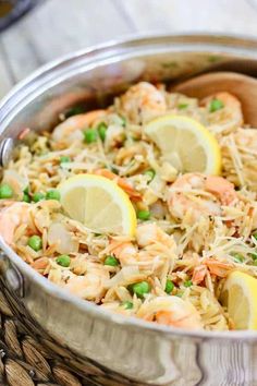 a pan filled with rice and shrimp next to lemon wedges on a wooden table