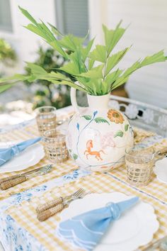 the table is set with plates, silverware and a vase filled with green plants