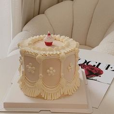 a white cake sitting on top of a table next to a magazine and cupcake