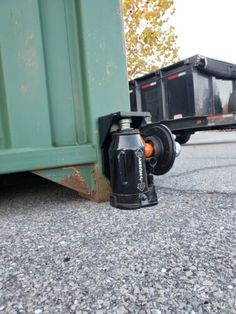 a close up of a metal object on the ground near a dumpster and trash can