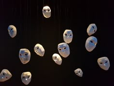 several masks hanging from strings in front of a black background with white faces on them