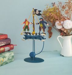 a table with books, vase and figurine on it next to some flowers