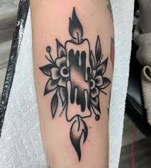 a black and white photo of a candle with flowers on the side of his arm