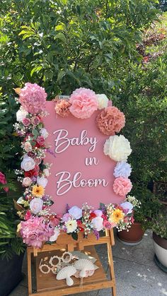 a baby in bloom sign surrounded by flowers and seashells on a easel