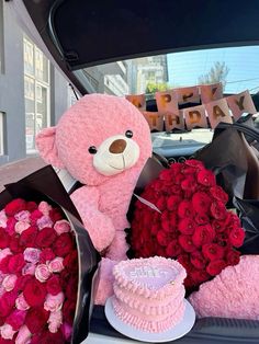 a pink teddy bear sitting in the back of a car next to roses and a cake