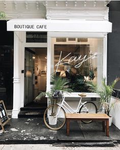 a white bicycle parked in front of a store window with potted plants on the sidewalk