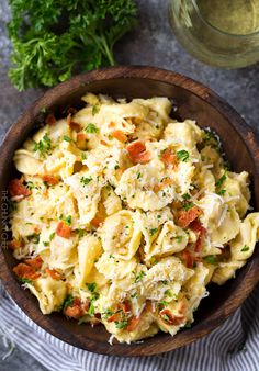 a wooden bowl filled with pasta salad next to a glass of wine and parsley