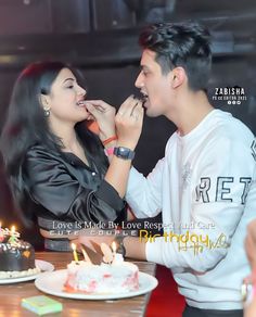 a man feeding a woman cake with candles on her face at a table in front of him