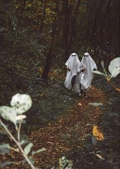 two people dressed in white walking through the woods