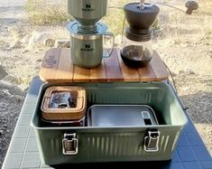 there is a coffee pot and two cups on top of an old suitcase with the lid open