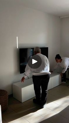 two men standing in front of a flat screen tv on top of a white entertainment center