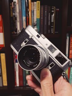 a person holding an old camera in front of a book shelf with books on it