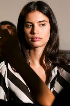 a woman with long brown hair and black and white striped shirt looking at the camera