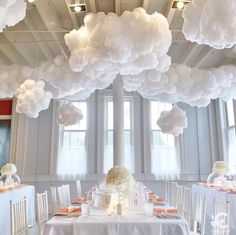 a room filled with white tables and chairs covered in paper clouds hanging from the ceiling