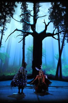 two people are dancing on stage in front of a tree and foggy forest background