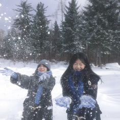 two girls are playing in the snow with their mitts and throwing snowballs into the air