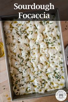 a pan filled with dumplings covered in cheese and herbs on top of a wooden table