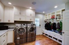 a washer and dryer in a large laundry room with white cabinets, wood flooring and open shelving