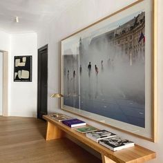 a large painting hanging on the wall above a wooden bench in a living room with hard wood flooring