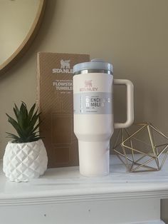 a white coffee cup sitting on top of a table next to a pineapple plant