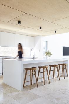 a woman is standing in the middle of a kitchen with stools and an island