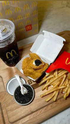 a wooden tray topped with french fries next to a cup of soda and ketchup