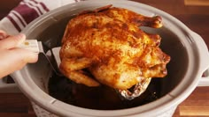 a person holding a fork in a pot filled with chicken and broth on top of a wooden table