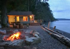 there is a fire pit in front of the house on the shore with chairs around it