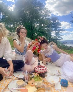 three women sitting on the ground with food and drinks in front of them at a picnic