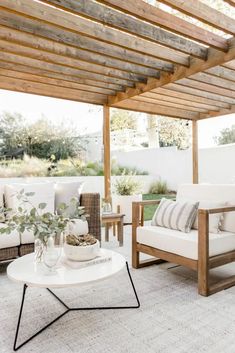 an outdoor living room with white furniture and wood beams on the ceiling, along with greenery