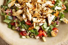 a salad with chicken, tomatoes, lettuce and other veggies in it