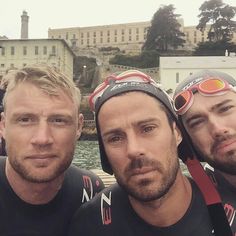 three men are posing for the camera in front of a body of water