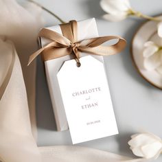 a white tag tied with a brown ribbon on top of a table next to flowers