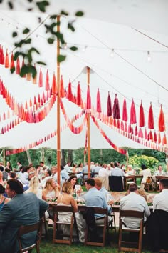 a group of people sitting around a table under a white tent with red tassels