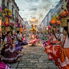 several women in colorful dresses carrying baskets on their heads down the street while others watch