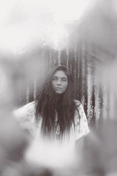 a woman with long hair standing in front of trees