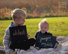 two young children sitting on top of a blanket holding signs that say oldest and youngest